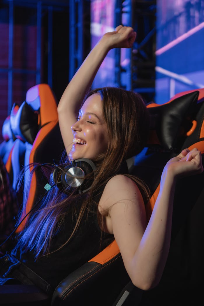 Smiling woman in gaming chair celebrating victory with arms raised, wearing headphones.