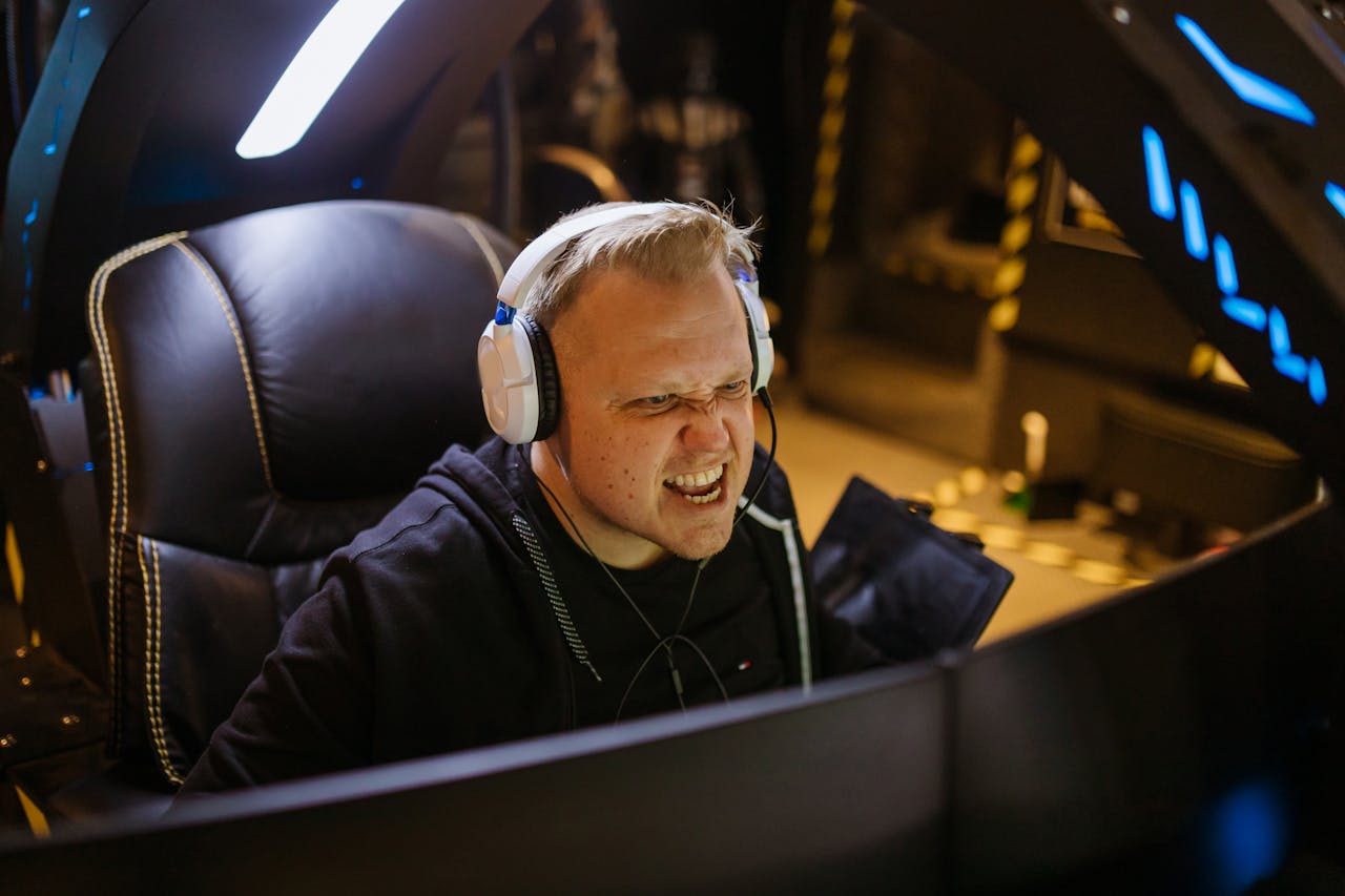 A passionate gamer celebrating victory while gaming indoors with white headphones and a gaming chair.